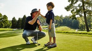 Adult high fiving a kid on the golf course